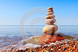 Rock zen pyramid of white pebbles in the pink rays of the rising sun against the calm summer sea