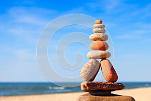 Rock zen pyramid of white and pink pebbles on a background of blue sky and sea.