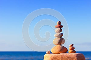 Rock zen pyramid of white and pink pebbles on a background of blue sky and sea.