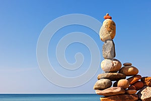 Rock zen pyramid of white and pink pebbles on a background of blue sky and sea