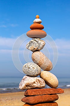 Rock zen pyramid of white and pink pebbles on a background of blue sky and sea