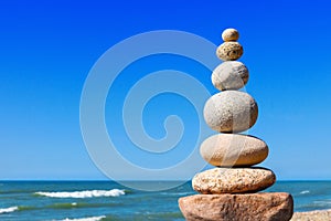 Rock zen pyramid of white and pink stones on a background of blue sky and sea.