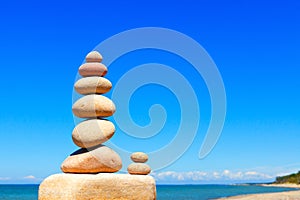 Rock zen pyramid of white and pink stones on a background of blue sky and sea.