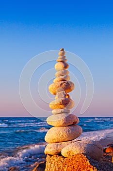Rock zen pyramid of white stones in the pink rays of the setting sun against the sea