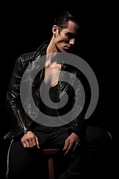 Rocker in black leather jacket posing seated in dark studio