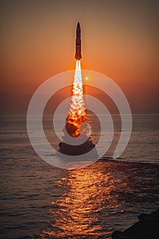 A rocket launching into the sky over the ocean at sunset