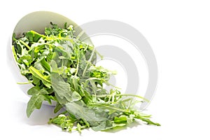 Rocket salad leaves, rucola or arugula, falling from a ceramic b