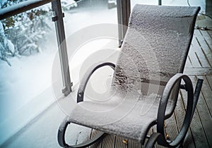 a rocking chair covered with snow on veranda, outdoor winter scenery