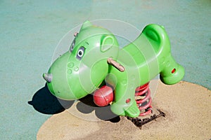 Rocking chair on a green metal spring made of plastic in the shape of a hippo on a playground with a rubberized coating.