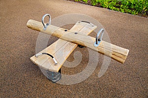 Rocking chair on a yellow metal spring made of natural logs and boards on a playground with a rubberized coating.