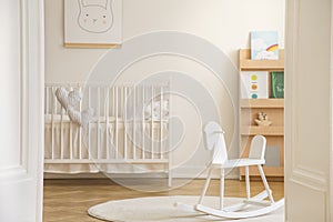 Rocking horse on rug in white kid`s bedroom interior with rabbit poster above cradle