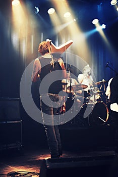 Rocking out. A guitarist on stage with his band beneath strobe lights in a nightclub.