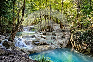 Rocks with cascading water make a series of beautiful short waterfalls in the dense forest of Erawan National park in