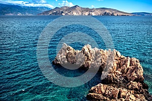 Rocks on cliffs and waves in the ocean, seen from a beach. Calm water, clear sky and waves on a sunny summer day