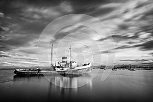 Rocks and a completely calm sea in the foreground with a ship aground with mountains in the background photo