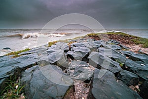 Rocks covered in mosses and surrounded by the wavy sea under a cloudy sky in the evening