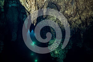 Rocks formation in an underwater cave with a silhouette view of scuba divers in the background