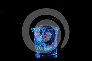 Rocks glass overflowing with water under bright blue lights with red on a black background