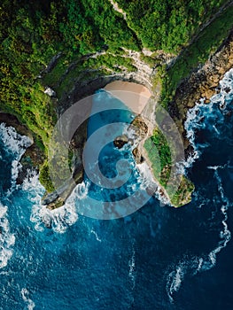 Rocks, little beach and blue ocean with waves in Bali. Aerial view