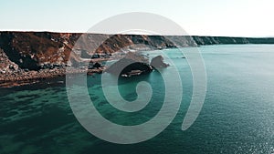 Rocks off the ocean coast line with turquoise water and dramatic cliffs Aerial view.