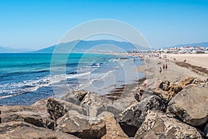 Rocks overlooking the sand and sea of Los Lances beach, silhouettes of bathers and mountain in the background, Tarifa SPAIN photo