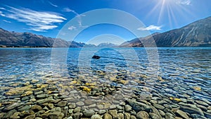 The rocks and pebbles under the surface on the foreshore of Lake Ohau with a background of the Southern Alps