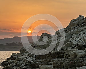 Rocks pile near the beach with big sun and orange sky