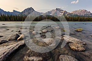 Rocks on a river with forest and mountains in the background along the Icefields Parkway in Jasper National park, Alberta, Canada