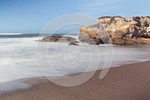 Rocks on a sand beach and blue ocean on horizon. Long exposure photography.