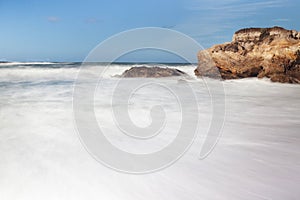 Rocks on a sand beach and blue ocean on horizon. Long exposure photography.