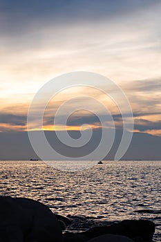 Rocks on the sand and fishermen in small fishing boats On the sunset background,silhouette