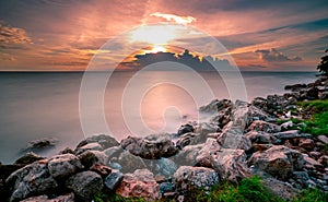 Rocks on stone beach at sunset. Beautiful landscape of calm sea. Tropical sea at dusk. Dramatic golden sunset sky and clouds.