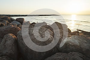 Rocks and stones on the beach with pier at sunrise