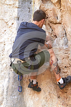 Rockstar of rock climbing. Rearview of a tattooed rock climber clinging onto a crack in the rockface.