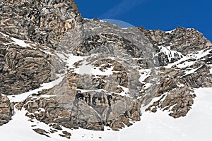 Rocky alpine mountainside with frozen waterfall