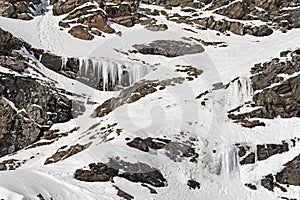 Rocky alpine mountainside with frozen waterfall