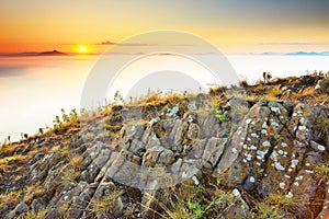 Rocky basalt peak on hill. Forest valley full of gentle fog and Sun above heavy mist.