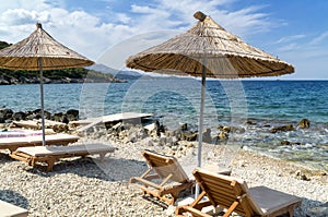 Rocky beach in Ksamil, Ionian Sea with sunbeds and straw umbrellas. Blue and tourquse sea in background, nobody.