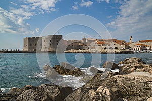 Rocky beach and sea waves on the background of ancient town with fortress