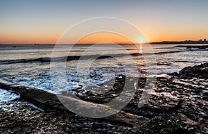 Rocky beach with small waves and a colorful sunset at the Atlantic Ocean in Estoril