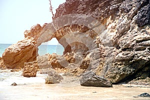 A rocky beach with a view of the rock with holes and the sea. Rocky cliffs and ocean waves on a sandy beach.