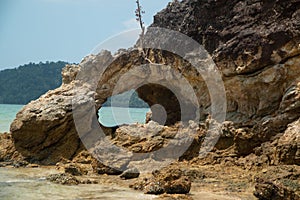 A rocky beach with a view of the rock with holes and the sea. Rocky cliffs and ocean waves on a sandy beach.