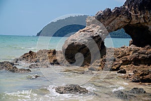 A rocky beach with a view of the rock with holes and the sea. Rocky cliffs and ocean waves on a sandy beach.