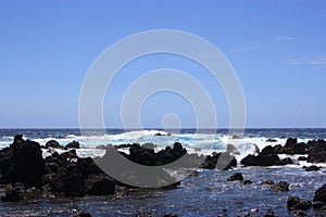Rocky, black lava shoreline fronting deep blue Pacific Ocean at Laupahoehoe Point with clear blue skies