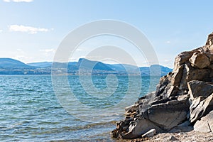 Rocky cliff face with view of Okanagan Lake and Giant`s Head mountain on sunny day