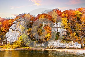 Rocky cliff with yellowed trees and mountain river in autumn