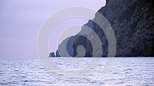 Rocky coast in cloudy weather on background of horizon. Shot. Rocks descend into calm sea in rainy cloudy weather