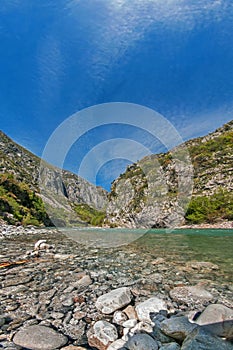 Rocky coast of a mountain river in the Balkans against a blue sky with feathery clouds