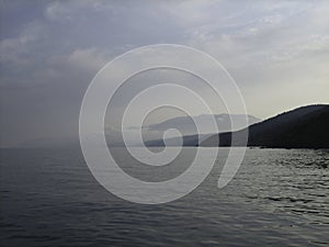 Rocky coast at sunset. In the distance, the coast mountains loomed in the mist