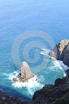 Rocky coastline of the Atlantic Ocean with waves and cliffs mountains and blue sky in Madeira Island, Portugal